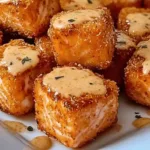 Golden crispy bang bang salmon bites drizzled with creamy spicy sauce on a white plate