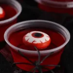 Red gelatin Halloween cups topped with candy eyeballs and a black plastic spider for spooky party treats.