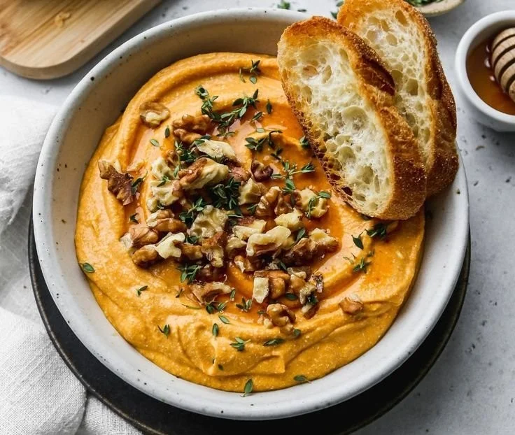 Pumpkin Whipped Feta Dip served in a bowl with crackers and garnished with herbs