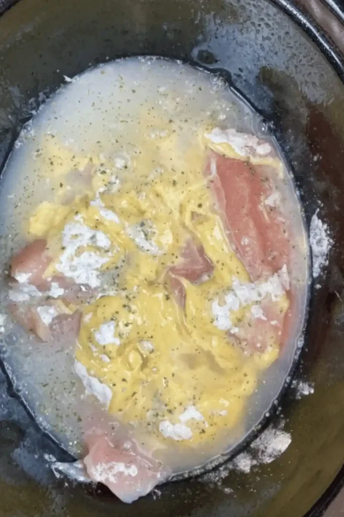 Pouring chicken broth into slow cooker with chicken and soup mixture