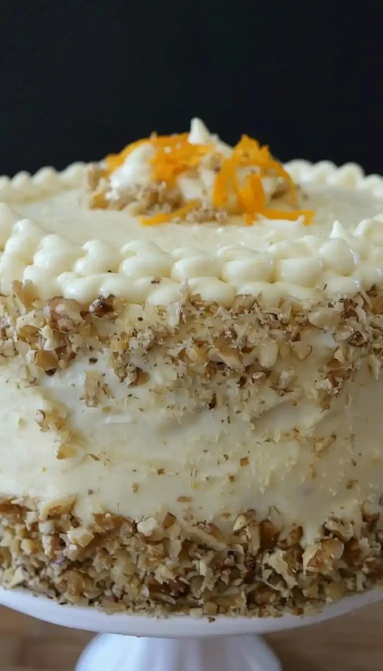 A slice of moist carrot cake recipe with cream cheese frosting and a sprinkle of nuts